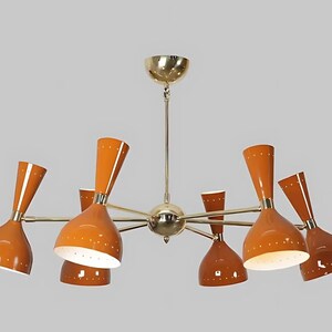 Könnte beinhalten: Ein Kronleuchter im Mid-Century-Modern-Stil mit acht orangefarbenen, kegelförmigen Schirmen. Die Schirme haben eine weiße Innenseite und goldfarbene Zierleisten. Die Leuchte hat eine goldfarbene Zentralkugel und Arme.