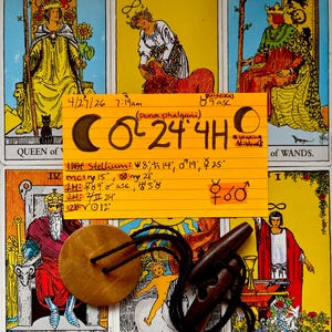 May include: A collection of tarot cards with a wooden pendant and a dark brown wooden whistle. A handwritten note with astrological symbols and text is placed on top of the cards. The cards feature illustrations and titles.
