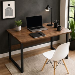 May include: A rectangular desk with a dark wood grain surface and black metal frame, featuring a laptop, a black notebook with a pen, a black desk lamp, a black cup, and a small potted plant. A white chair with wooden legs sits in front.