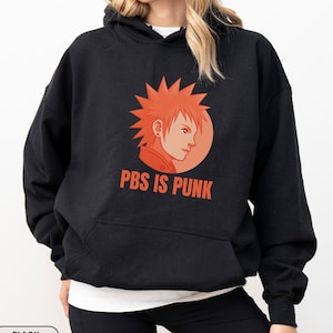 May include: Black hoodie with a front pocket. The design features an orange graphic of a spiky-haired character and the text "PBS IS PUNK" in orange. The sweatshirt is black.