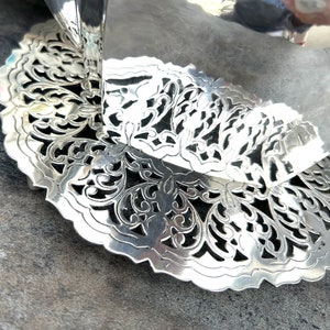 May include: A silver, decorative, openwork, circular tray with a scalloped edge. The tray has a delicate, floral design.