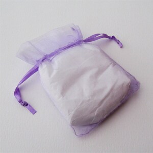 May include: A small, sheer lavender gift bag with a white interior. The bag is tied with a matching lavender ribbon. The bag is made of a soft, translucent material.