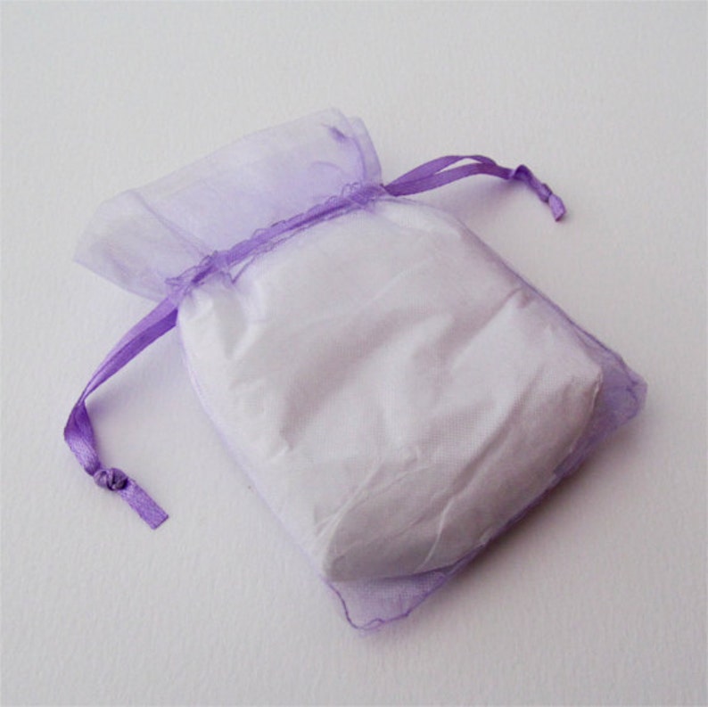 May include: A small, sheer lavender gift bag with a white interior. The bag is tied with a matching lavender ribbon. The bag is made of a soft, translucent material.