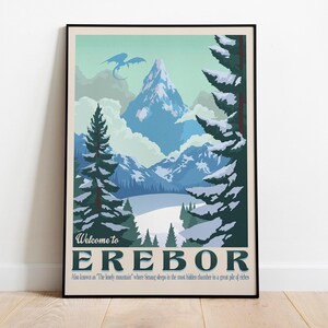 May include: A framed poster featuring a mountain landscape with a dragon silhouette in the sky. The poster has a vintage travel aesthetic, with text that reads "Welcome to Erebor". The color palette includes blues, greens, and white.