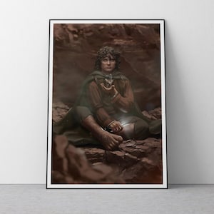 May include: Framed art print featuring a seated figure in a brown tunic and green cloak, holding a glowing object. The artwork has a fantasy theme, set against a rocky, earthy background. The print is displayed in a black frame.