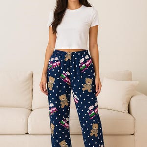 Könnte beinhalten: Marineblaue Schlafanzughose mit einem sich wiederholenden Muster aus Teddybären, Geschenken und weißen Punkten. Die Hose hat einen Kordelzug in der Taille. Das Model trägt ein weißes Crop-Top.