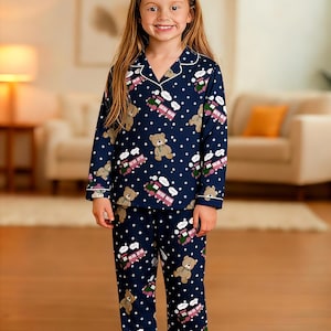 May include: Navy blue pajama set with a repeating pattern of teddy bears, trains, and white polka dots. The long-sleeved top and pants have white trim. The pajamas are made of a soft material.