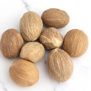 May include: Close-up of whole nutmegs, displaying a textured, light brown surface. The spices are arranged on a white background, highlighting their natural appearance. Suitable for culinary applications.