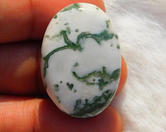 Pode incluir: Pedra preciosa oval com base branca e intrincados padrões verdes semelhantes a musgo. A pedra polida é segurada na mão, mostrando sua superfície lisa e design natural. Uma pedra decorativa única para joias ou coleção.
