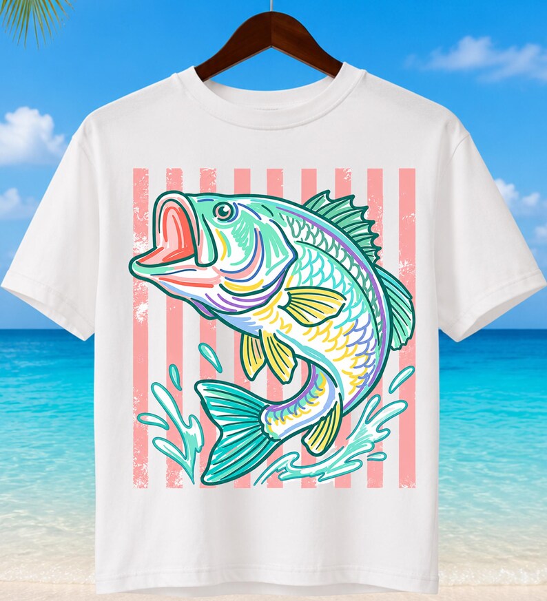 May include: White t-shirt featuring a colorful illustration of a largemouth bass jumping out of water. The fish is depicted in shades of teal, yellow, purple, and pink, set against a background of pink and white vertical stripes. The shirt is hanging on a wooden hanger.