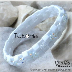 May include: White tile bangle bracelet with sparkling crystal accents. The bracelet has a square tile design and is decorated with iridescent crystals. The word "Tutorial" is visible on the bracelet. The bracelet is a jewelry item.