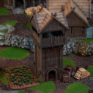 Könnte beinhalten: Ein detailliertes Miniatur-Wachturm aus Holz mit Strohdach, umgeben von anderen Miniaturgebäuden und einem kleinen Garten. Der Turm hat einen Balkon mit Holzpfosten und einen kleinen Bogeneingang. Die Szene befindet sich auf einer grünen und braunen Oberfläche.