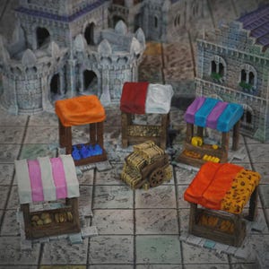 Pode incluir: Bancas de mercado em miniatura com toldos coloridos, exibindo diversos produtos. As bancas são feitas de madeira e apresentam toldos laranja, vermelho, branco, rosa, azul e roxo. Há também um carrinho de feno em miniatura, com estruturas de castelo ao fundo.
