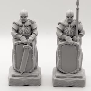Pode incluir: Duas figuras de cavaleiros cinzentos, uma com espada e escudo, a outra com lança e escudo. Ambas usam capacetes e armaduras, em bases semelhantes a pedra. As figuras têm desenhos detalhados e estão em fundo branco.