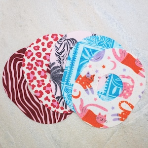 Könnte beinhalten: Eine Sammlung von fünf kreisförmigen Klebepflastern mit verschiedenen Mustern, darunter dunkelrote Zebrastreifen, ein rot-rosa Leopardenmuster, ein schwarz-weißes Palmenblattdesign, ein blaues Blumenmotiv und ein weißer Hintergrund mit orangefarbenen Katzen.