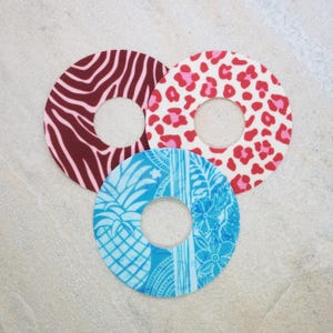May include: Three circular adhesive patches with a center hole. One patch features a dark red and light pink zebra stripe pattern, one has a red and pink leopard print, and the third displays a blue and light blue pineapple and floral design.
