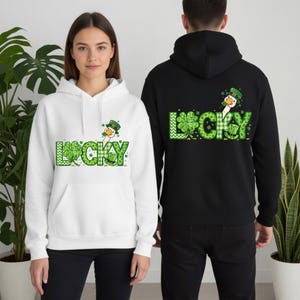 May include: White and black hoodies with a St. Patrick's Day theme. The hoodies feature the word "LUCKY" in green with a shamrock design and a cartoon goose wearing a leprechaun hat. The white hoodie is on the front, and the black hoodie is on the back.