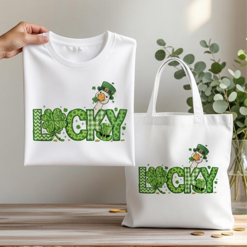 May include: White t-shirt and tote bag featuring a green and white design with the word "LUCKY" and a cartoon goose wearing a green hat. The design includes shamrocks and a leprechaun hat, perfect for St. Patrick's Day.