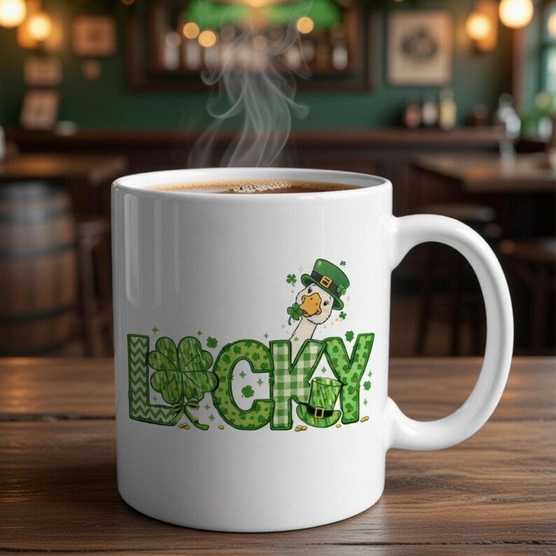May include: White ceramic mug with a St. Patrick's Day theme. The mug features the word "LUCKY" in green with shamrock and plaid patterns, and a cartoon goose wearing a green hat. The mug is filled with hot coffee.