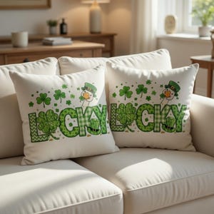 May include: Two white throw pillows with a St. Patrick's Day theme. Each pillow features the word "LUCKY" in green, with shamrocks and a cartoon duck wearing a green hat. The pillows are on a white couch.