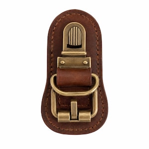May include: A brown leather strap connector featuring a rounded shape with visible stitching along the edges. The center is equipped with a brass-toned metal buckle, a rectangular loop, and a spring-loaded clip mechanism for secure attachment.