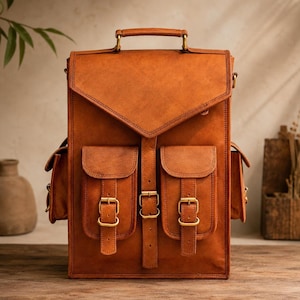 May include: A tan leather backpack featuring a large top flap with a handle, two front pockets with buckle closures, and a central vertical strap with a buckle. The design includes side pockets and brass-toned metal hardware throughout.