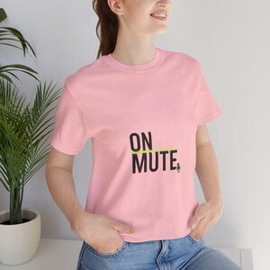 May include: A light pink t-shirt with the words "ON MUTE" printed in black. A green line underlines the word "MUTE", and a small microphone icon is to the right. The shirt is short-sleeved and made of a soft material.