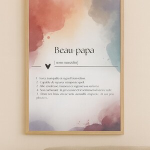 May include: Framed art print with the text "Beau-papa" and a definition in French. The background features watercolor-style splashes of red, purple, and blue. The wooden frame adds a classic touch.