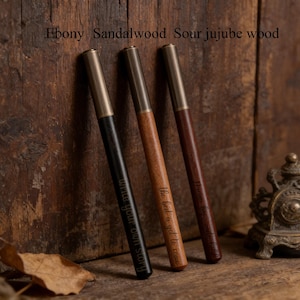 May include: Three wooden pens with brass-colored tips and accents. The pens are made of ebony, sandalwood, and sour jujube wood. The black pen reads "write your own story", the brown pen reads "the best is yet to come", and the dark brown pen reads "embrace the journey".