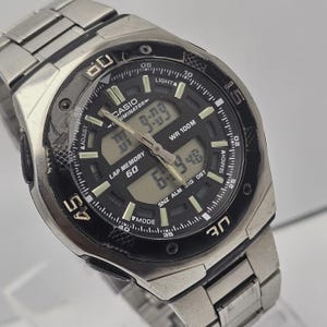 May include: A silver-toned Casio digital watch with a black face. The watch displays the time and has a stainless steel band. The watch face includes the text "CASIO", "WR 100M", and other function indicators.
