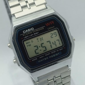 Puede incluir: Un reloj digital Casio plateado con esfera negra y azul. El reloj muestra la hora 2:57:47 PM, la fecha 29, y presenta el texto "CASIO", "ALARM CHRONO" y "WATER RESIST". La correa del reloj es de metal plateado.