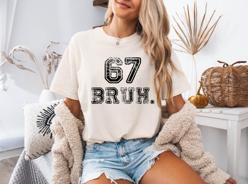 May include: Cream-colored t-shirt with the number "67" and the word "BRUH" printed in black, distressed lettering. The shirt is a casual style, suitable for everyday wear.