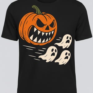 May include: Black t-shirt featuring a Halloween design. An orange pumpkin with a menacing face and sharp teeth is paired with three white cartoon ghosts. The design includes speed lines, suggesting movement.