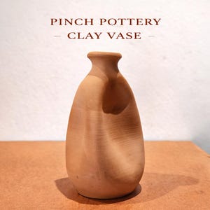 K&ouml;nnte beinhalten: Eine handgefertigte Vase aus Ton in nat&uuml;rlicher Terrakotta-Farbe. Die Vase hat eine einzigartige, organische Form mit schmalem Hals und breiterem K&ouml;rper. Der Text "PINCH POTTERY - CLAY VASE -" ist oben im Bild zu sehen.