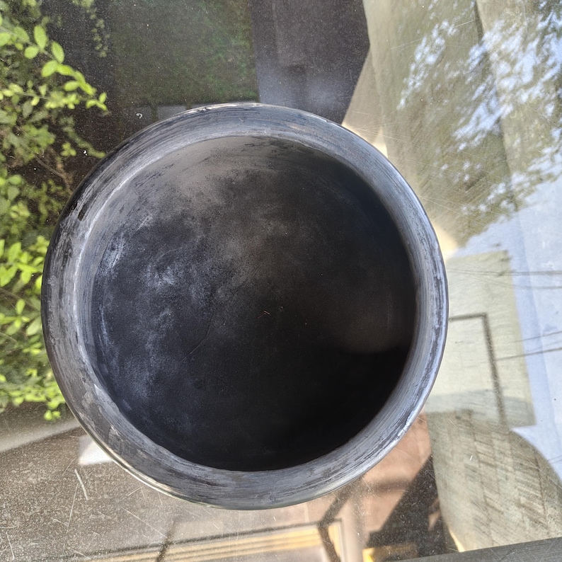 May include: A dark grey, round ceramic bowl with a wide rim. The bowl has a textured surface and appears to be empty. The bowl is sitting on a reflective surface.