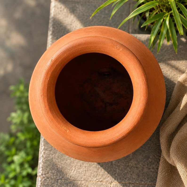 May include: A top-down view of a terracotta pot featuring a wide, circular opening and a smooth, rounded rim. The vessel is crafted from natural clay, displaying a warm, earthy orange-brown color with a matte, unglazed finish and a deep interior.