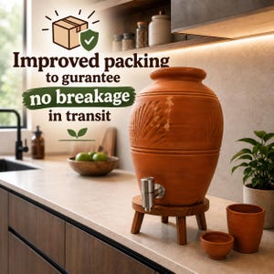 May include: A terracotta water dispenser with a silver metal spigot, resting on a small wooden stand. The vessel features carved leaf patterns and is accompanied by a matching terracotta cup and small bowl. Text reads: Improved packing to gurantee no breakage in transit.