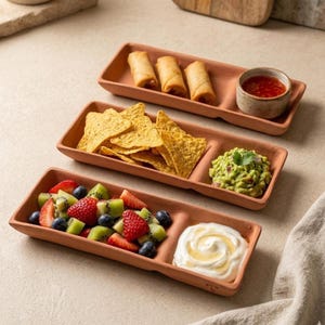Puede incluir: Tres bandejas de servicio de terracota llenas de comida. La bandeja superior contiene rollitos de primavera y un cuenco pequeño con salsa roja. La bandeja del medio tiene totopos y guacamole. La bandeja inferior contiene fruta y crema.