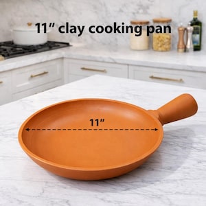 May include: An 11-inch clay cooking pan with a handle. The pan is a warm terracotta color and sits on a white countertop. The text "11" is displayed across the diameter of the pan. The pan is designed for cooking.