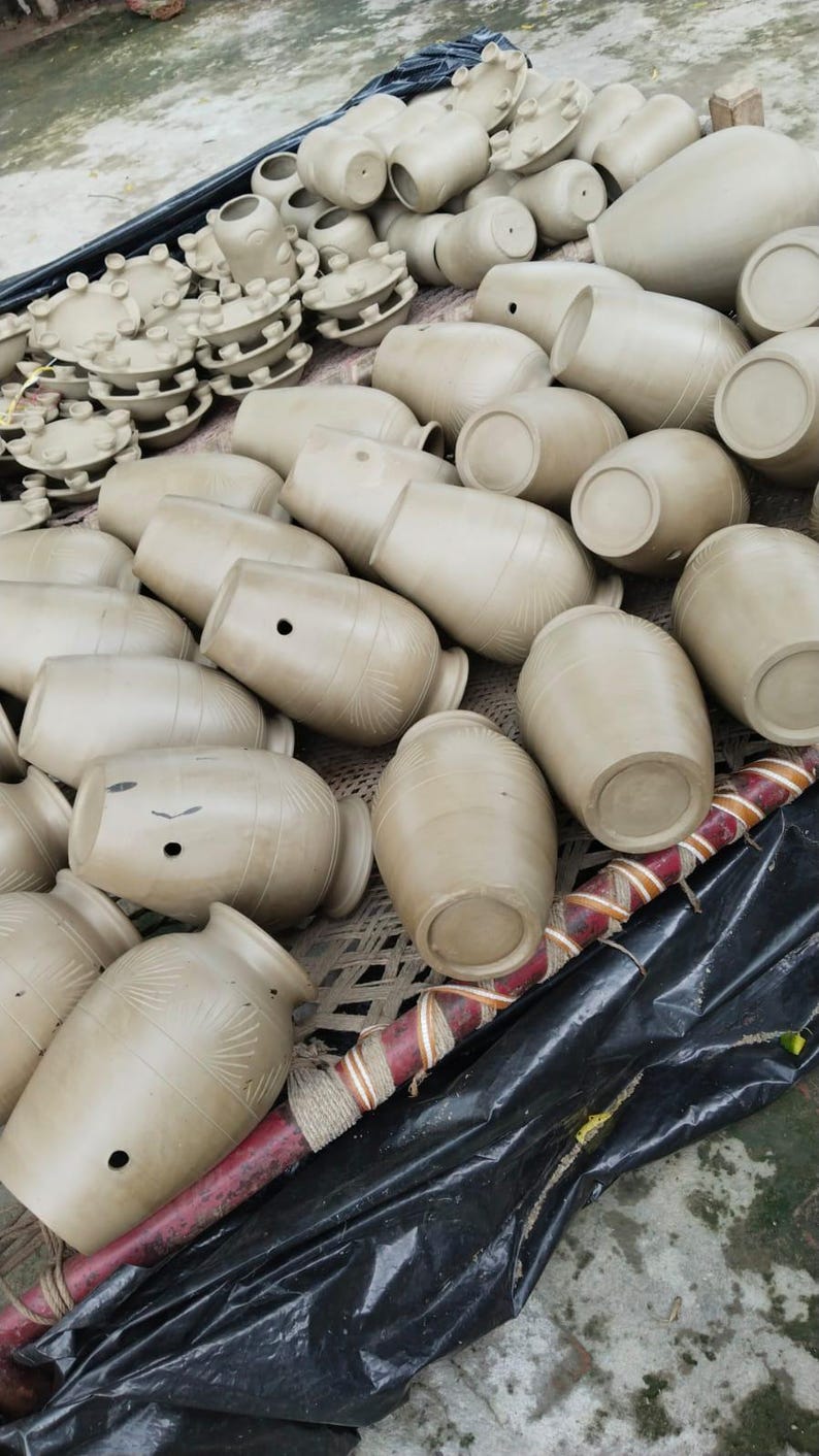 May include: A large collection of unglazed, light brown clay vessels and small circular pottery components. The vessels feature rounded bodies, narrow necks, and small circular openings on the sides, with some displaying subtle etched fan-like patterns.