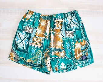 May include: Teal and brown patterned shorts with an elastic waistband. The shorts feature a repeating design of geometric shapes, palm trees, and boats. The fabric has a soft, slightly faded appearance. The shorts are laid flat on a white wooden surface.