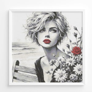 Puede incluir: Retrato en blanco y negro de una mujer con labios rojos y cabello rubio corto y ondulado. Sostiene un ramo de flores blancas y una rosa roja. El fondo muestra una escena de playa.