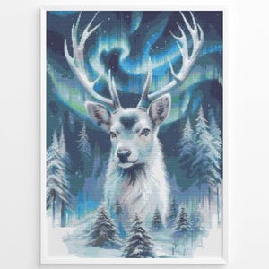Op de afbeelding: Ingelijst kunstwerk met een witte hert met groot gewei, tegen een achtergrond van een besneeuwd bos en het noorderlicht. Het kleurenpalet omvat blauw, groen en wit, waardoor een serene winterscène ontstaat.