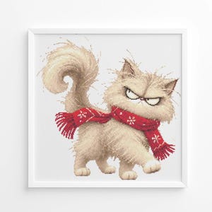May include: A framed cross-stitch pattern featuring a fluffy, light beige cat with a grumpy expression. The cat has a long, curved tail and is wearing a bright red scarf decorated with white snowflake patterns, all set against a plain white background.