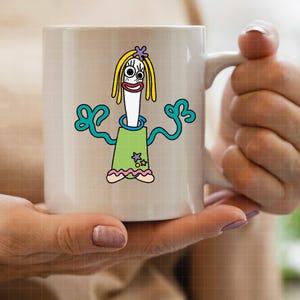 Pu&ograve; includere: Tazza in ceramica bianca con un design di personaggio dei cartoni animati stravagante. Il personaggio ha un corpo bianco, capelli gialli e un vestito verde. Il design include braccia turchese e un fiore viola. La tazza &egrave; tenuta da una persona.