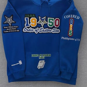 May include: Royal blue hooded sweatshirt with embroidered patches. Patches include text and graphics related to the Order of the Eastern Star, including "1950 Order of Eastern Star" and "Covered OES". The sweatshirt also features the text "Ladies of Deborah #053".