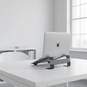Könnte beinhalten: Ein silberner Laptop steht auf einem grauen Laptop-Ständer auf einem weißen Schreibtisch. Auf dem Ständer steht das Wort "prexun". Der Hintergrund ist eine weiße Wand und ein Fenster.