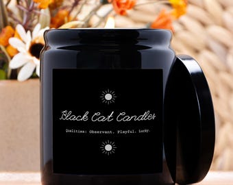 Może przedstawiać: Czarna świeca w szklanym słoiku z pokrywką, oznaczona jako "Black Cat Candles". Etykieta zawiera cechy: Obserwator, Zabawny, Szczęśliwy. Świeca jest zapalona, z widocznym płomieniem. Tło obejmuje kwiaty i tkaną fakturę.