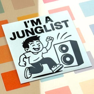 Peut inclure: Un autocollant blanc avec le texte "I'M A JUNGLIST" en noir. L'autocollant présente une illustration de dessin animé d'une personne courant avec le poing levé, à côté d'un haut-parleur.