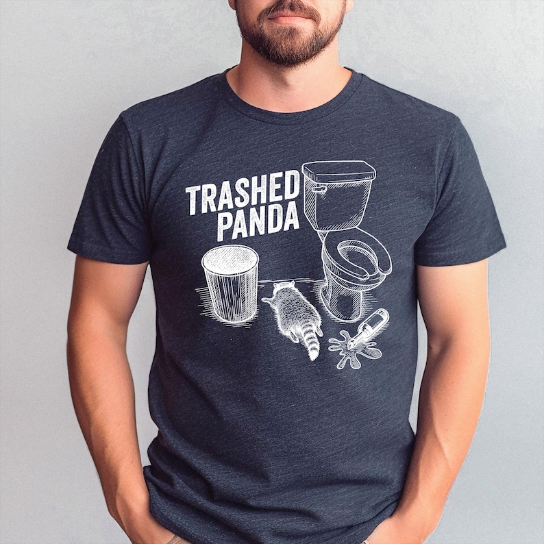 May include: Dark gray t-shirt with a white graphic of a raccoon, toilet, trash can, and spilled bottle, with the text "Trashed Panda". The design is a humorous illustration.